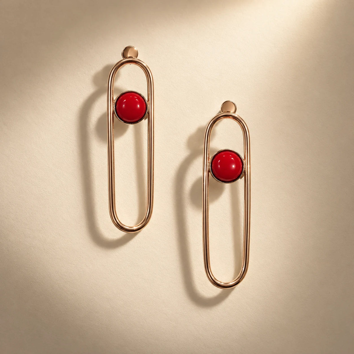 Sleek oval drop earrings in 18k gold plated metal with a bold red coral accent. Ankkshi's Aakar collection.
